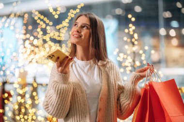 Sihirli dekorasyonlar, telefonla konuşmak. Yeni yıl alışverişi ve hediyeleri. Kadın Noel ağacının yanında..
