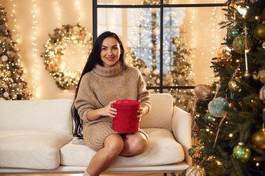 Mutlu kadın yeni yıl hediyesiyle kanepede oturuyor..