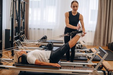 Uzanmak ve bacak egzersizi yapmak. Kadın eğitmen yaşlı kadına yardım ediyor..