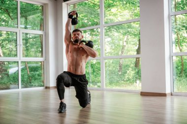 Pencerelere yaslanın. Dambıllı. Güçlü kaslı adam spor salonunda çalışıyor..