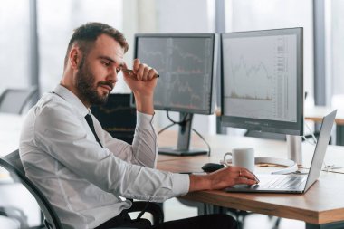 Yan görüş. İşadamı bilgisayar başında oturuyor ve ofiste çalışıyor..