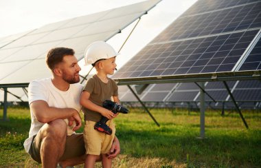 Başlık ve matkapla. Baba ve küçük oğlu güneş panellerinin yakınındalar..