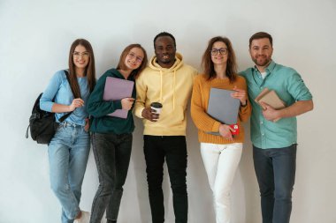 Not defterleri ve kahve fincanı tutuyor. Bir grup genç beyaz arka planda duruyor..