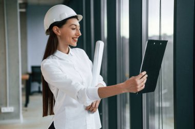 Plan ve not defteri elimde. Kasketli ve beyaz elbiseli kadın mimar içeride..