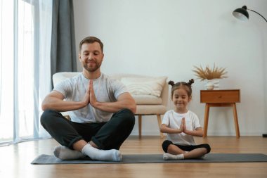 Küçük kızı olan baba evde yoga yapıyor..