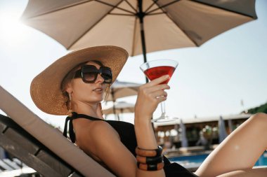 Yan görünüş, elinde kokteyl ile uzanmak. Güzel genç bayan tatil köyünde..