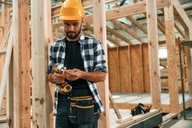 Turuncu renkli matkap ve kasket ellerinde. Ahşap depoda sanayi işçisi..