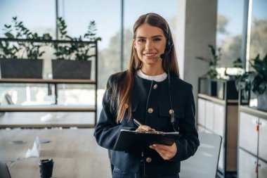 Kulaklıklı ve not defterli bir kadın ofiste bekliyor..