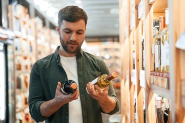 Ön manzara. Adam dükkanda şarap seçiyor..