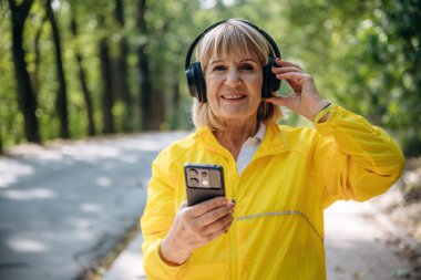 Modern akıllı telefon elinde. Sarı spor ceketli son sınıf öğrencisi kulaklıklarla dışarıda bekliyor..