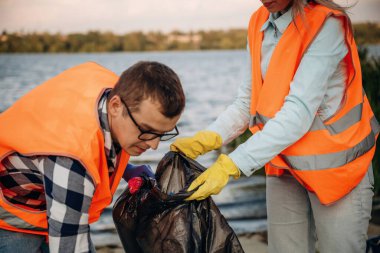 Çöp torbalarıyla. Bir gönüllü çamurlu bir sahilde çöp topluyor..