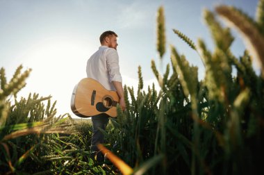Gitar ellerinde. Beyaz gömlekli adam tarlada..