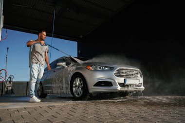 Gümüş renkli yüzey, otomobili yıkıyor. Adam dışarıda arabasıyla bekliyor..