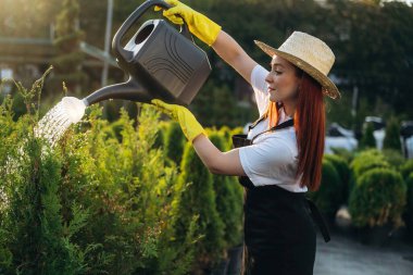 Plastikten yapılmış siyah sulama kutusu. Genç kızıl saçlı kadın bahçeyle ilgileniyor..