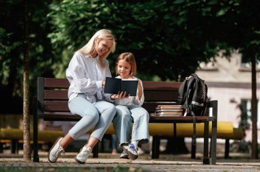 Öğrenmek ve birlikte okumak. Annesiyle küçük bir kız dışarıda bankta oturuyor..