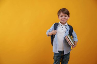 Okul için hazır, elinde kitaplarla. Küçük çocuk sarı arka planda stüdyoda..