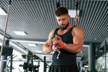 Elinde kırmızı koruyucu bandajlar var. Güçlü kaslı adam spor salonunda çalışıyor..