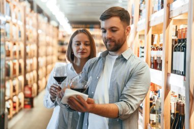 İçkili bardaklar. Örnek al. Erkek ve kadın dükkanda şarap seçiyorlar..