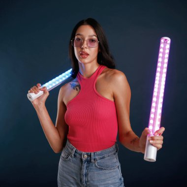 Neon ışıklandırma ekipmanları ellerinde. Güzel genç bayan arka plana karşı..