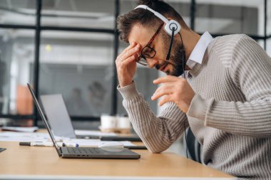 Yorgunum, kötü hissediyorum. Adam ofiste dizüstü bilgisayarın yanında oturuyor, iş kavramı..