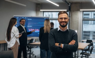 Kollarını kavuşturup meslektaşlarına karşı durarak. Bir grup ofis çalışanı içeride birlikte..