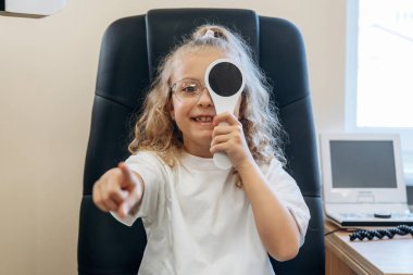 Küçük kız göz doktorunun dolabında görüşünü kontrol ediyor..