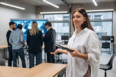 Bir kadının elinde not defteri. Bir grup ofis çalışanı içeride birlikte..