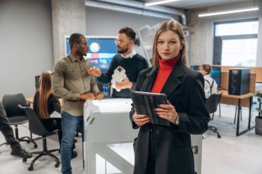 Dijital tablet ellerinde. Ofiste 3D yazıcının yanında insanlar var..