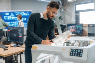 Beyaz baskılı nesneler ellerinde. Ofiste 3D yazıcının yanında insanlar var..