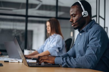 Kulaklıkla ve dizüstü bilgisayarlarla. Çağrı merkezinde insanlar çalışıyor..