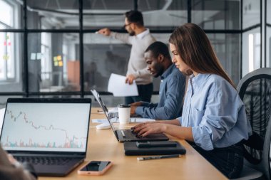 Adam camın yanında duruyor, bilgi veriyor. Profesyonel işçiler modern ofiste birlikte çalışıyorlar..