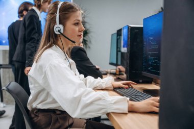 Kulaklıkla, bilgisayarın yanında oturuyor. Tasarımcı takımı ofiste birlikte..