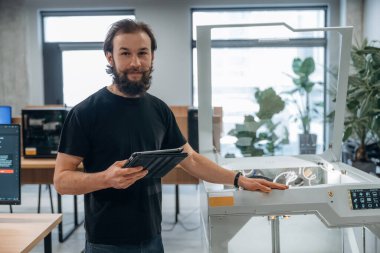 Ayakta, çalışıyor. Adam 3D yazıcıyla ofiste..