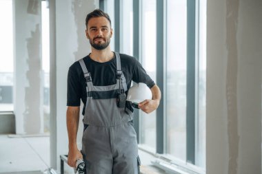 Gri üniformalı ve siyah gömlekli. Bir adam bitmemiş bir odayı yeniliyor..