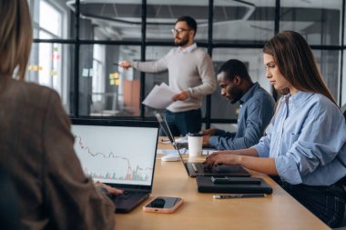 Adam camın yanında duruyor, bilgi veriyor. Profesyonel işçiler modern ofiste birlikte çalışıyorlar..