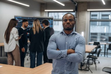 Afrikalı Amerikalı adam meslektaşlarına karşı duruyor. Bir grup ofis çalışanı içeride birlikte..