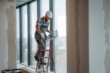 Pencerelerin yanında. Bir adam bitmemiş bir odayı yeniliyor..