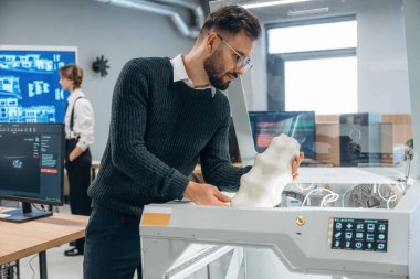 Beyaz baskılı nesneler ellerinde. Ofiste 3D yazıcının yanında insanlar var..