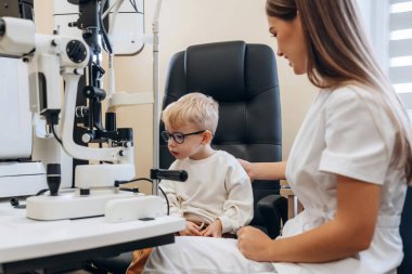 Gözlüklü olan. Küçük çocuk göz doktorunun dolabını kontrol ediyor..