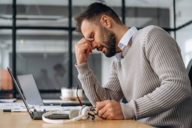 Yorgunum, kötü hissediyorum. Adam ofiste dizüstü bilgisayarın yanında oturuyor, iş kavramı..