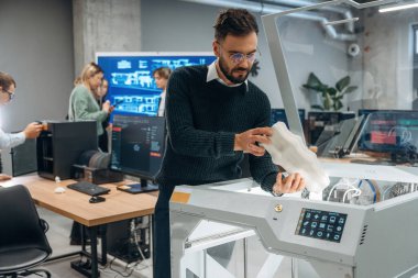 Beyaz baskılı nesneler ellerinde. Ofiste 3D yazıcının yanında insanlar var..