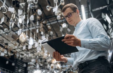 Tavanda bir sürü avize var. Erkek hırdavatçı dükkanında çalışıyor..