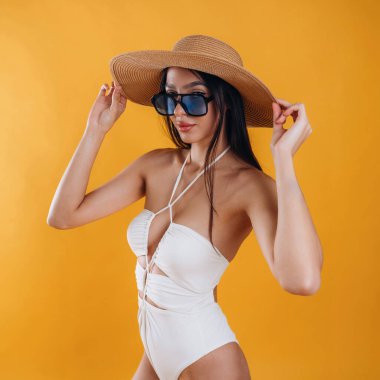 Yan görünüş, ayakta, güneş gözlüğü ve hasır şapkayla. Genç ve güzel bir turist kadın arka plana karşı..