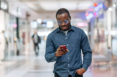 Ön manzara, elinde akıllı telefonla. Siyah adam süpermarketin holünde..