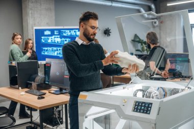 Beyaz baskılı nesneler ellerinde. Ofiste 3D yazıcının yanında insanlar var..