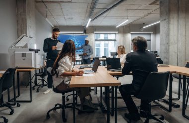 İnşaat planı ekranda. Bir grup ofis çalışanı içeride birlikte..