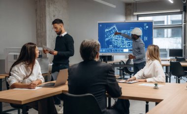 İnşaat planı ekranda. Bir grup ofis çalışanı içeride birlikte..