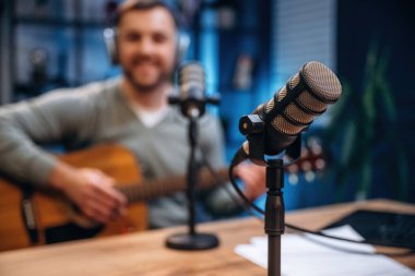 Kulaklıkla gitar çalıyor. Stüdyoda mikrofonu olan bir adam, podcast kavramı.