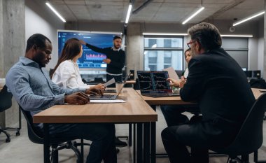 Büyük ekranda bilgi gösteriliyor. Bir grup ofis çalışanı içeride birlikte..