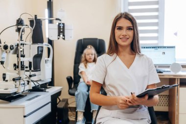 Elinde not defteriyle. Göz doktoru kliniğinde doktorla küçük bir kız..